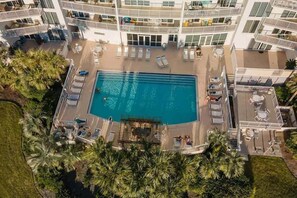 An aerial view of a hotel with a central swimming pool surrounded by sun loungers and a palm tree-lined deck. - Terrace At Pelican Beach 0804 3 Bedroom Condo (Destin)