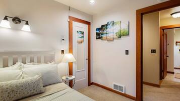 A hotel room with a bed, a nightstand, a lamp, a painting, and a door leading to another room.
