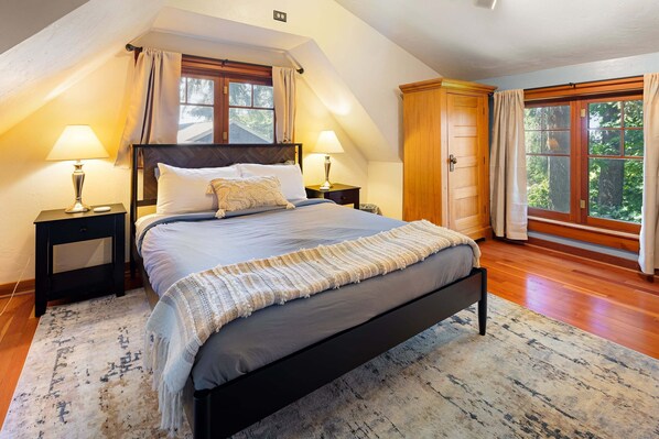 Un dormitorio con una cama grande, dos mesitas de noche, un armario de madera y una ventana con cortinas.
