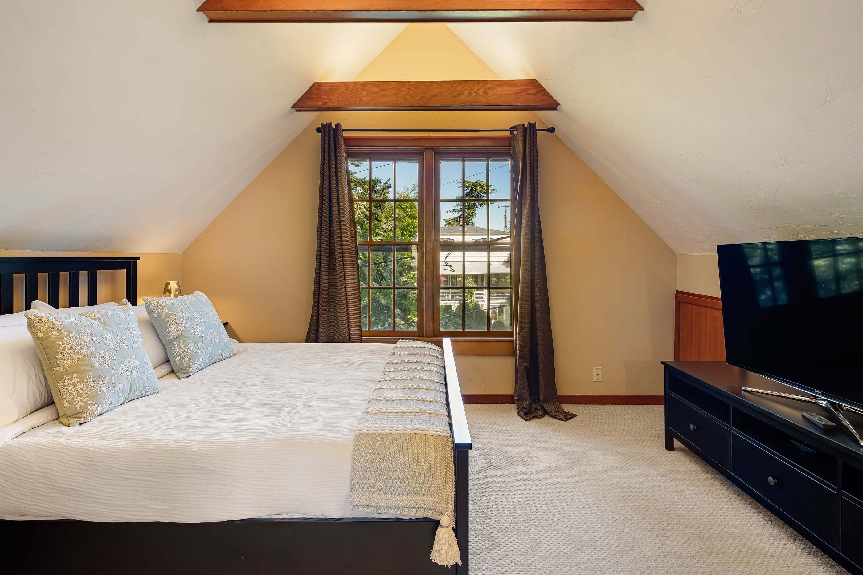 A bedroom with a bed, a television, and a window with curtains.