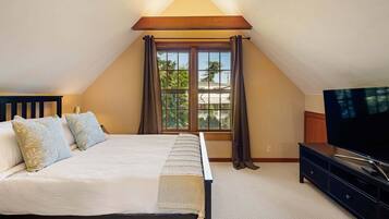 A bedroom with a bed, a television, and a window with curtains.