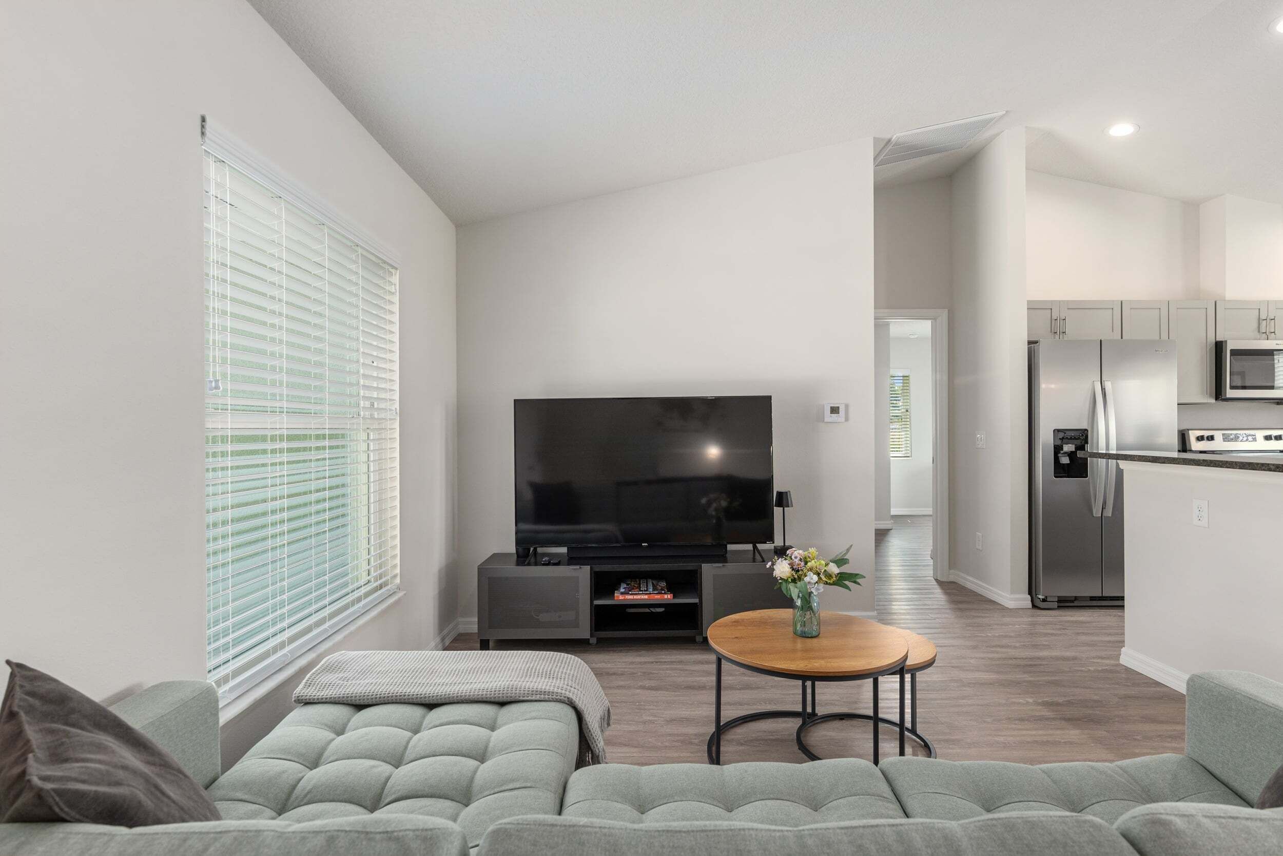 Een moderne woonkamer met een grijze bank, een flatscreen televisie en een klein houten tafeltje met een bloevas.