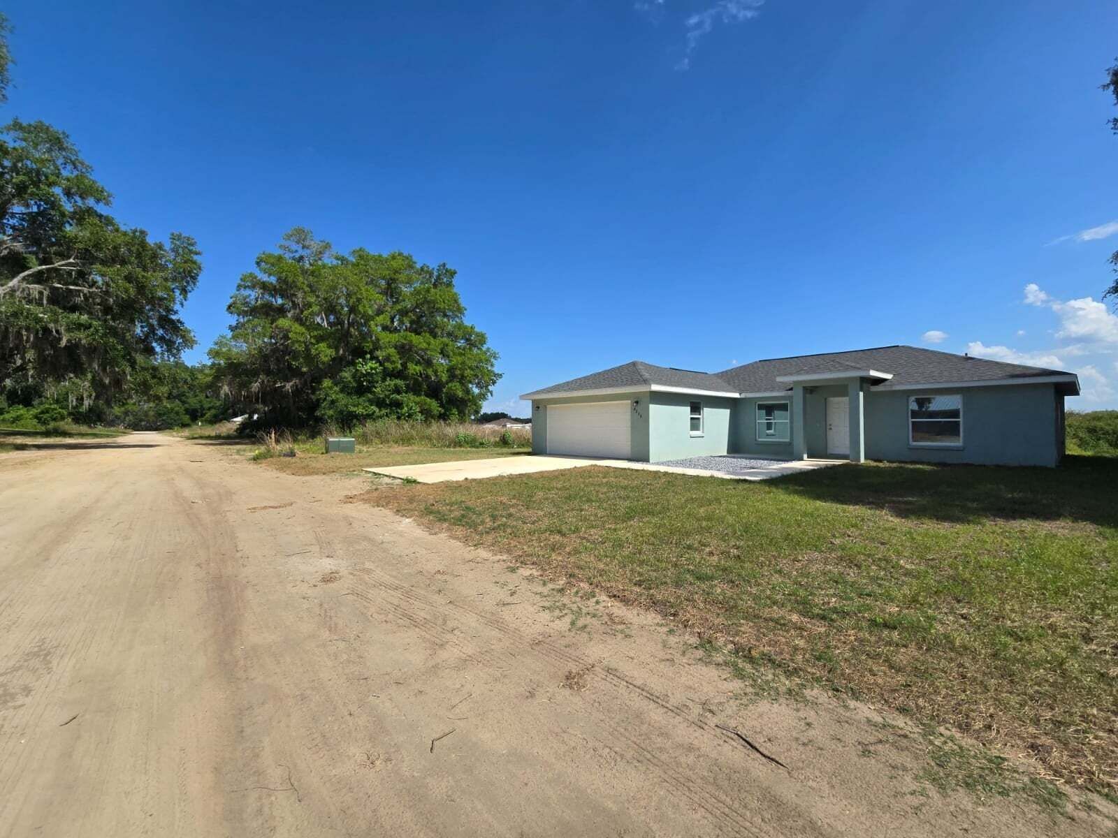 A single-story house with a garage, a front yard, and a dirt road.