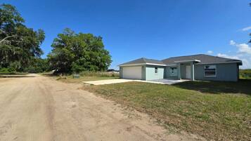 A single-story house with a garage, a front yard, and a dirt road.