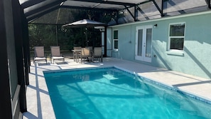 Ein Schwimmbecken mit überdachtem Patio, Gartenmöbeln und einem Haus mit Fensterläden.