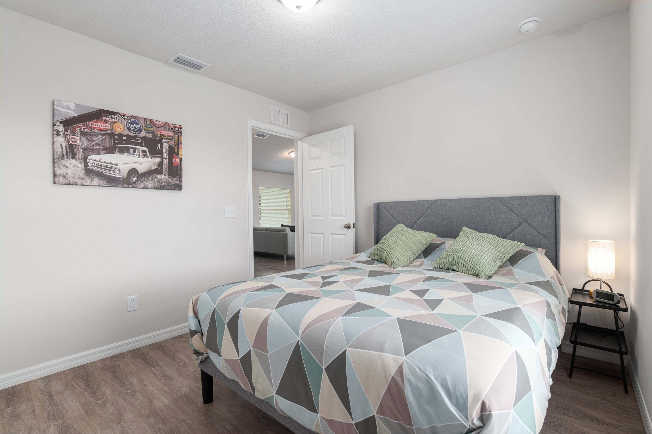 A bedroom with a bed, a nightstand, a lamp, and a door leading to another room.