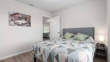 A bedroom with a bed, a nightstand, a lamp, and a door leading to another room.