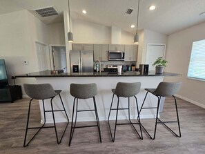 A modern kitchen with a central island, bar stools, and a potted plant. - Moments From The Trail Pool Villa 3 Bedroom Home (Inverness)