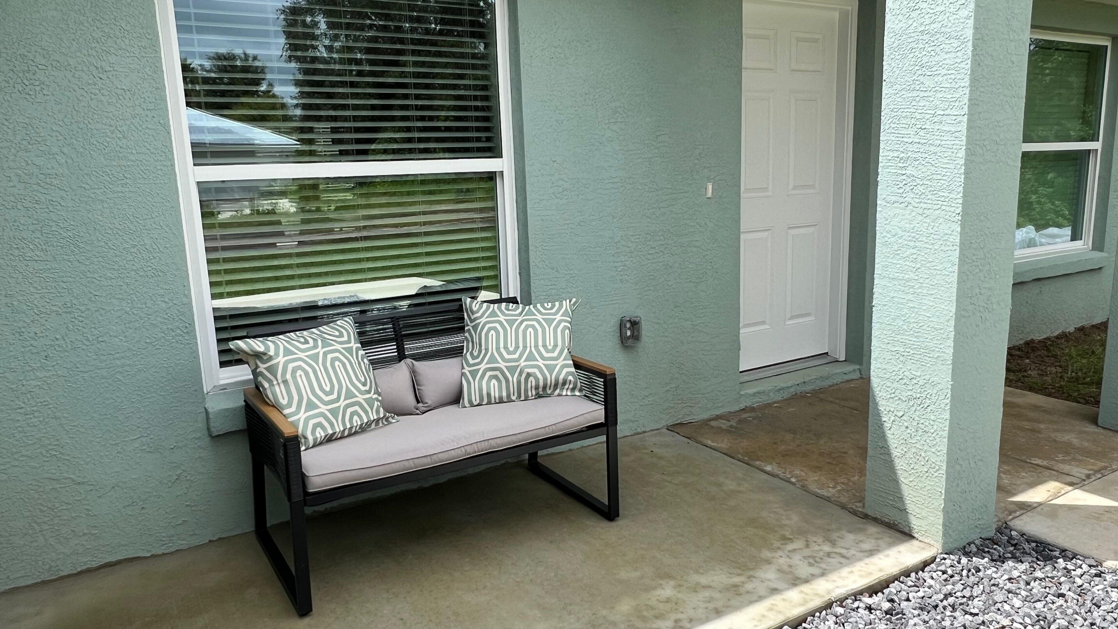 A bench with cushions outside a building with a door and window.