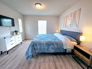 A bedroom with a bed, a dresser, a TV, and artwork on the wall. - Moments From The Trail Pool Villa 3 Bedroom Home (Inverness)