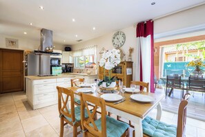A well-lit kitchen with modern appliances, a dining area with wooden chairs and a table set for two, and a view of the outside through large windows. - Charming ground floor villa apartment with a heated swimming pool (Cers)