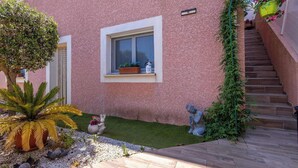 Ein pinkfarbenes Gebäude mit einem Fenster, ein kleiner Garten mit einer Palme und einer Statue.