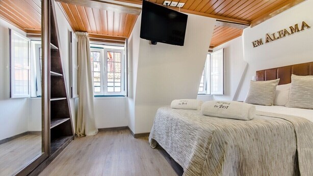 A bedroom with a bed, a TV, a window, and a wooden ceiling. - Alfama The Best Iii, in Old Lisbon (Lisbon)