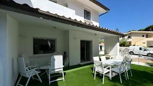 Un patio con mobiliario blanco y césped artificial verde.