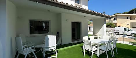 Un patio con mobiliario blanco y césped artificial verde.