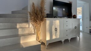 Una sala de estar moderna con una escalera, un televisor de pantalla plana, un armario blanco y plantas decorativas.