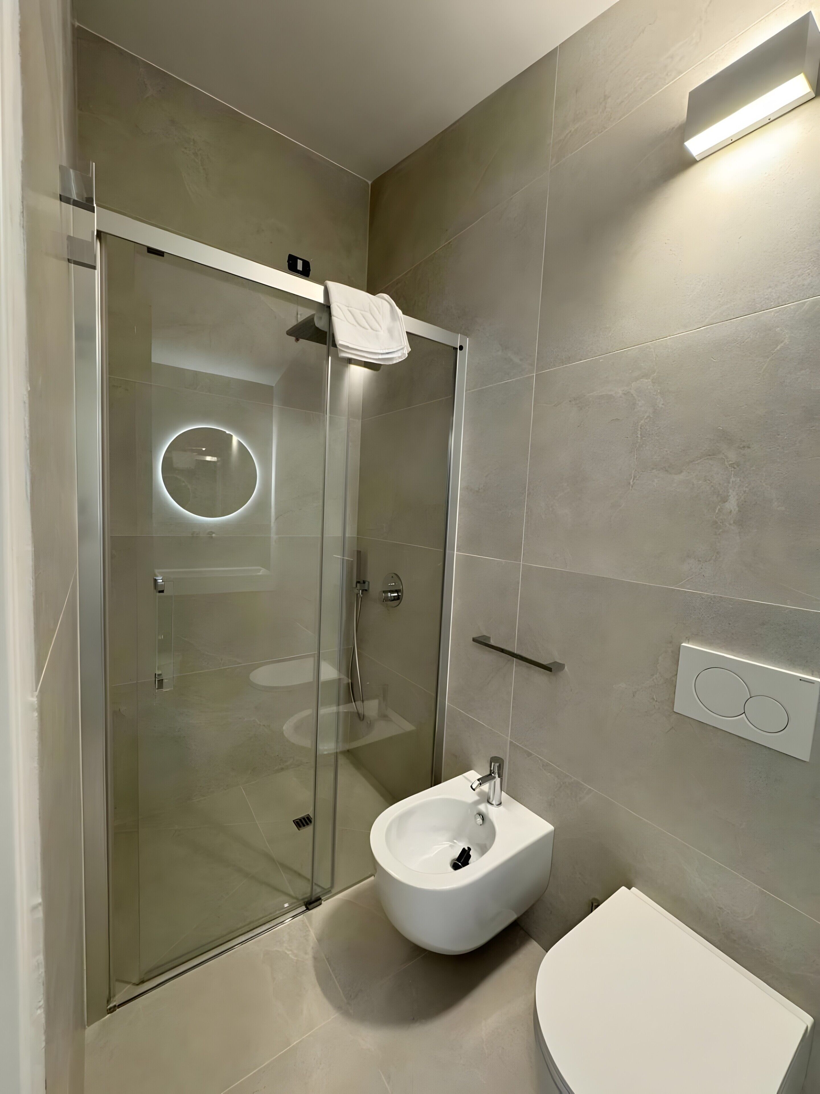 A modern bathroom with a glass-enclosed shower, a white pedestal sink, and a wall-mounted light fixture.
