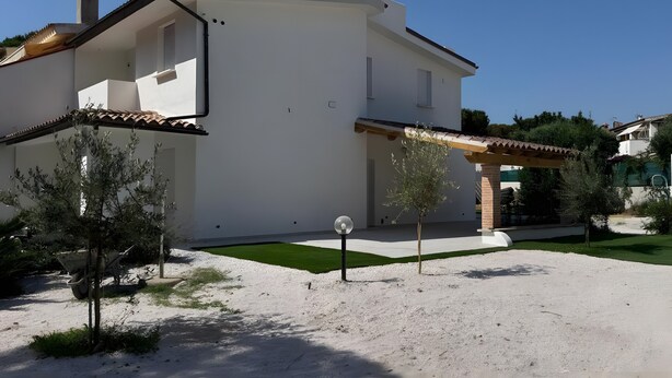 Una casa de dos pisos con fachada blanca, techo de tejas y un pequeño jardín con entrada de grava.