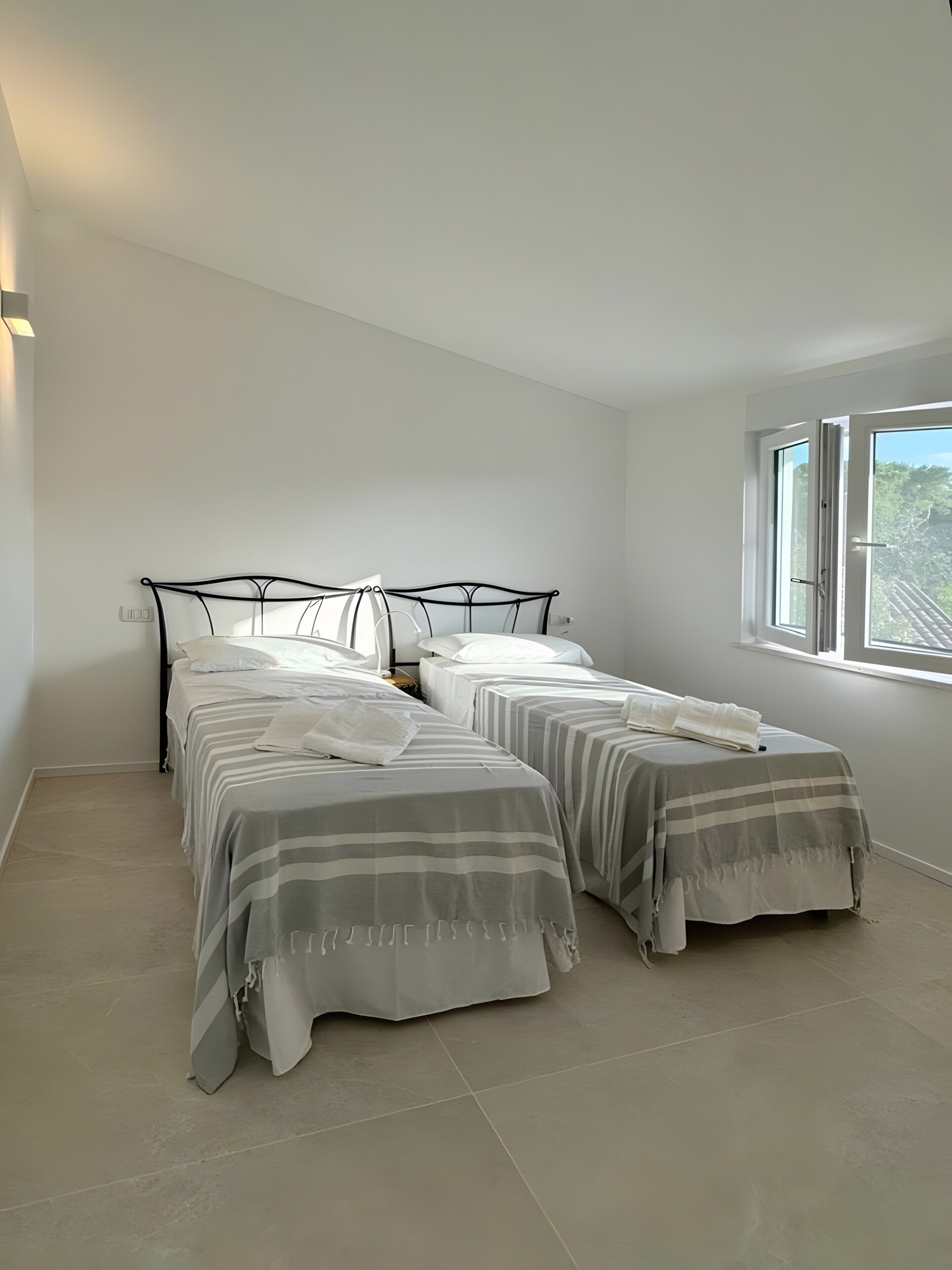 A bedroom with two beds, a window, and a light switch on the wall.