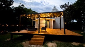A wooden deck with outdoor seating, a covered area with string lights, and a building with a triangular roof.