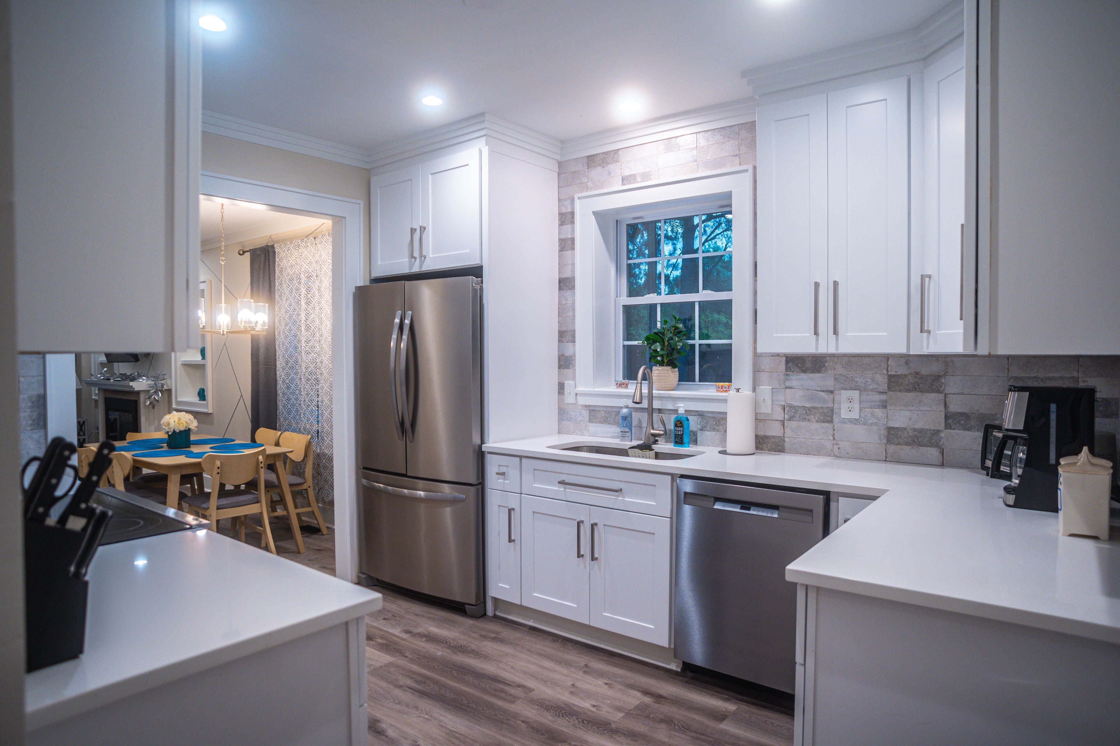A modern kitchen with stainless steel appliances, white cabinetry, and a window with a view of trees.