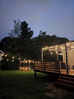 Un espacio de estar al aire libre techado, con luces colgantes, un banco de madera y una mesa.