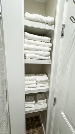 A white storage closet with shelves holding neatly folded white towels.