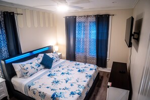 Een hotelkamer met een bed, een nachtkastje, een aan de muur bevestigde televisie en een raam met gordijnen.
