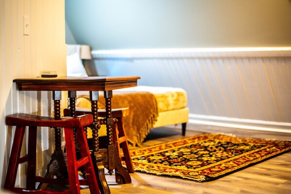 Una habitación con una cama, una silla de madera, una mesita pequeña y una alfombra estampada.