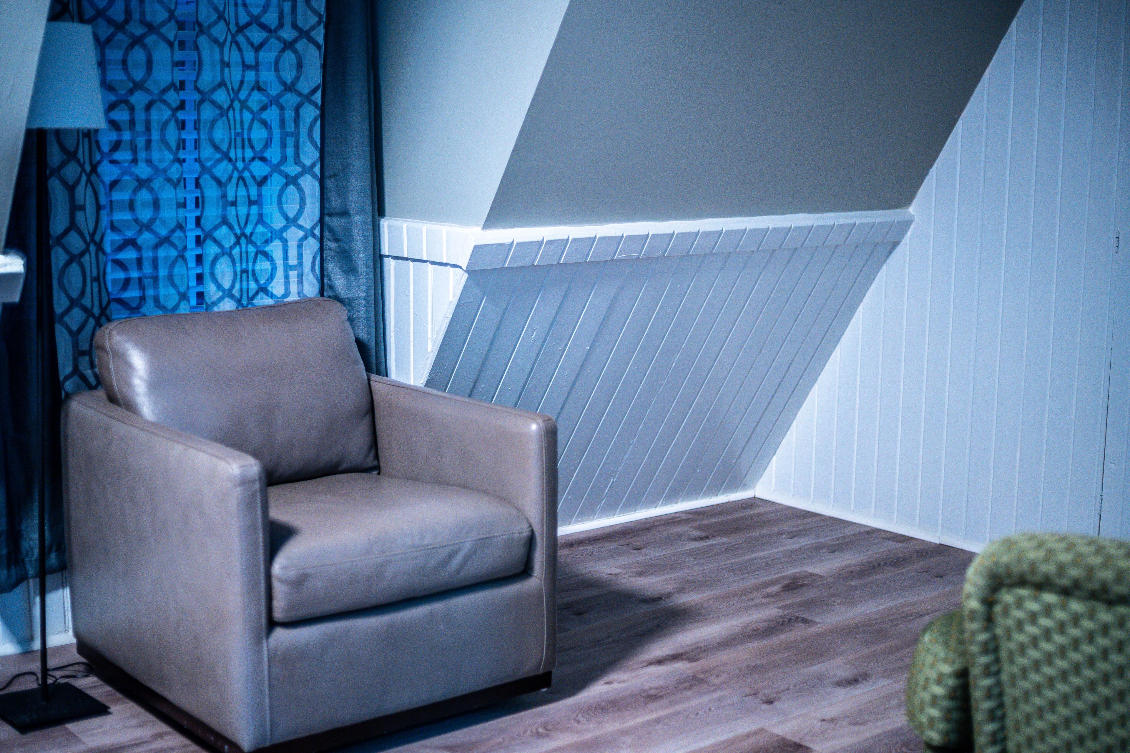 Una habitación con un sillón de cuero marrón, una lámpara y una cortina estampada.