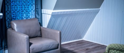 Una habitación con un sillón de cuero marrón, una lámpara y una cortina estampada.