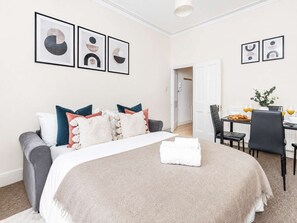 Een hotelkamer met een bed, een bureau met ontbijt en lijstjes met kunstwerken aan de muur.