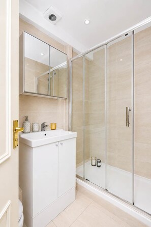 Un bagno moderno con box doccia in vetro, lavandino bianco con accessori dorati e specchio sopra al lavandino.