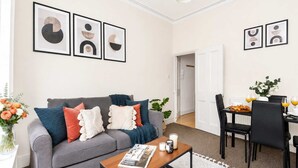 Ein modernes Wohnzimmer mit einem grauen Sofa, einem Couchtisch und einem Essbereich mit Stühlen sowie einem Tisch, der für das Frühstück gedeckt ist.
