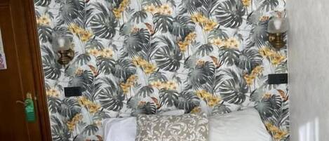 Un dormitorio con papel tapiz estampado, una cama con cubrecama estampado y una mesita de noche con una lámpara.