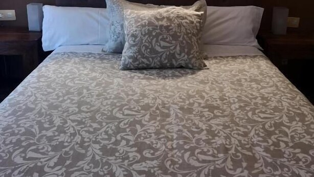 A bed with a patterned bedspread and two pillows, flanked by wall-mounted lights. - Hostal Plaza (Segovia)