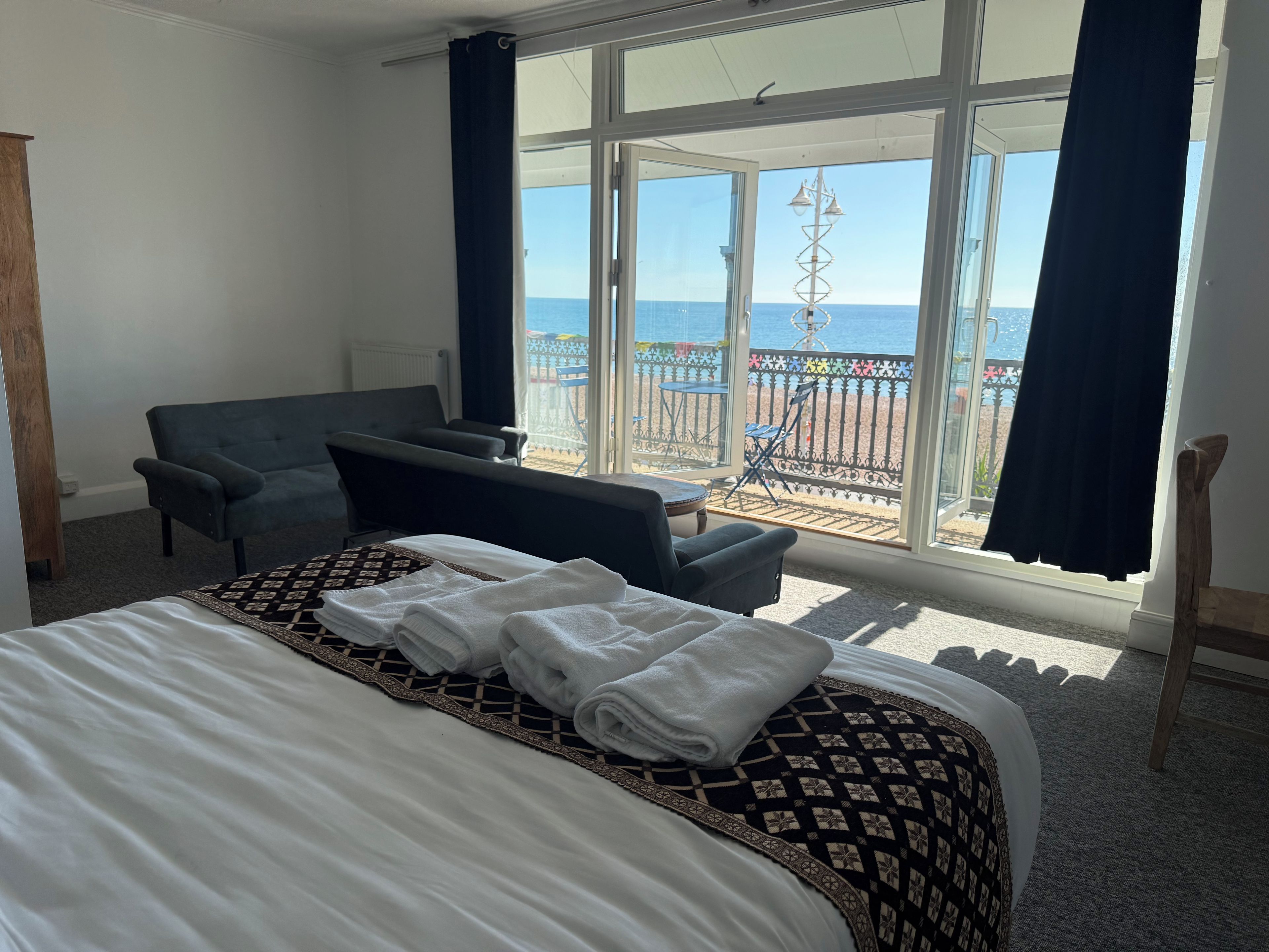 Habitación de hotel con cama, sofá, mesa y vista al mar a través de amplias ventanas.
