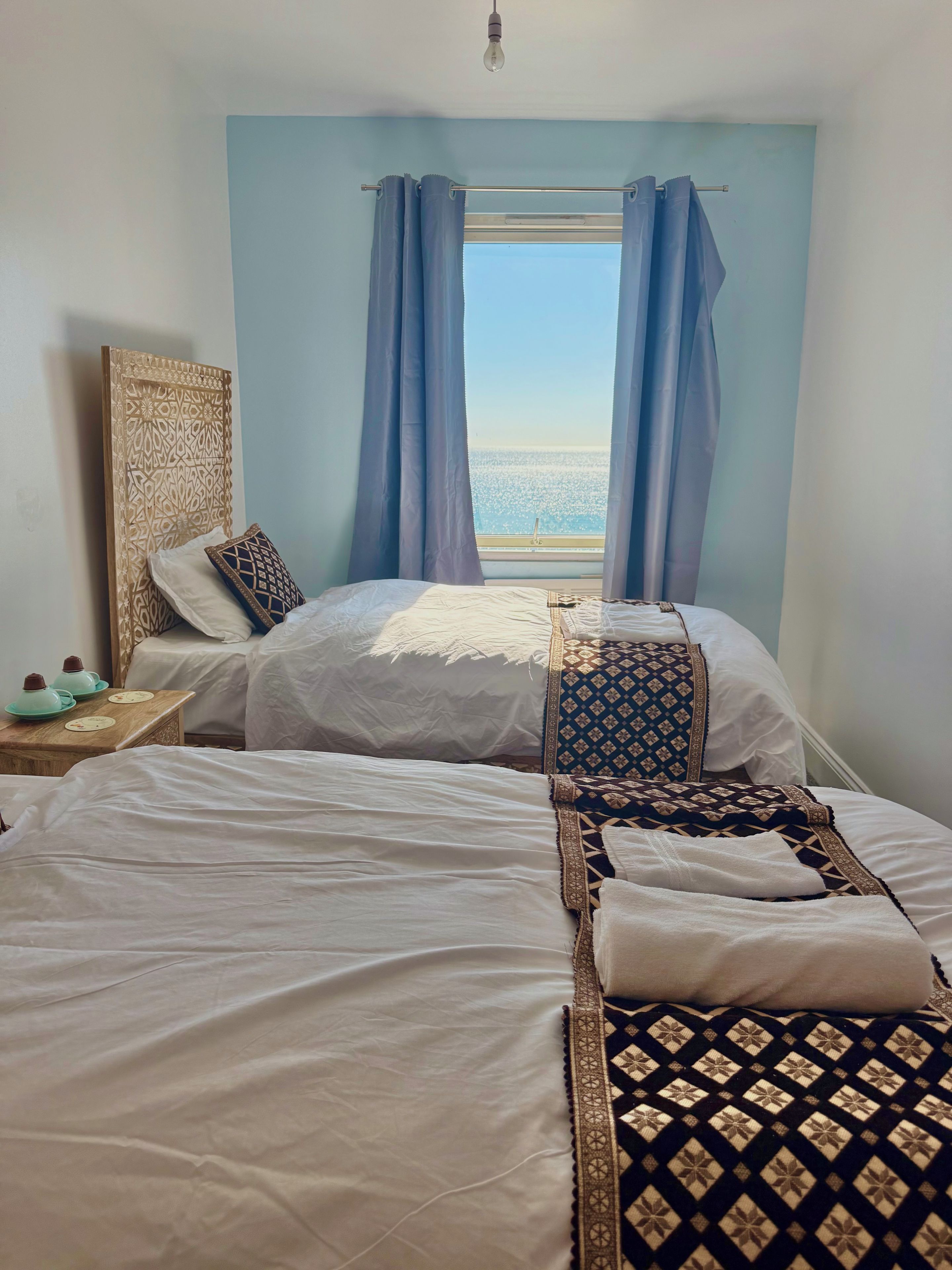 A hotel room with two beds, a view of the sea, and a window with curtains.