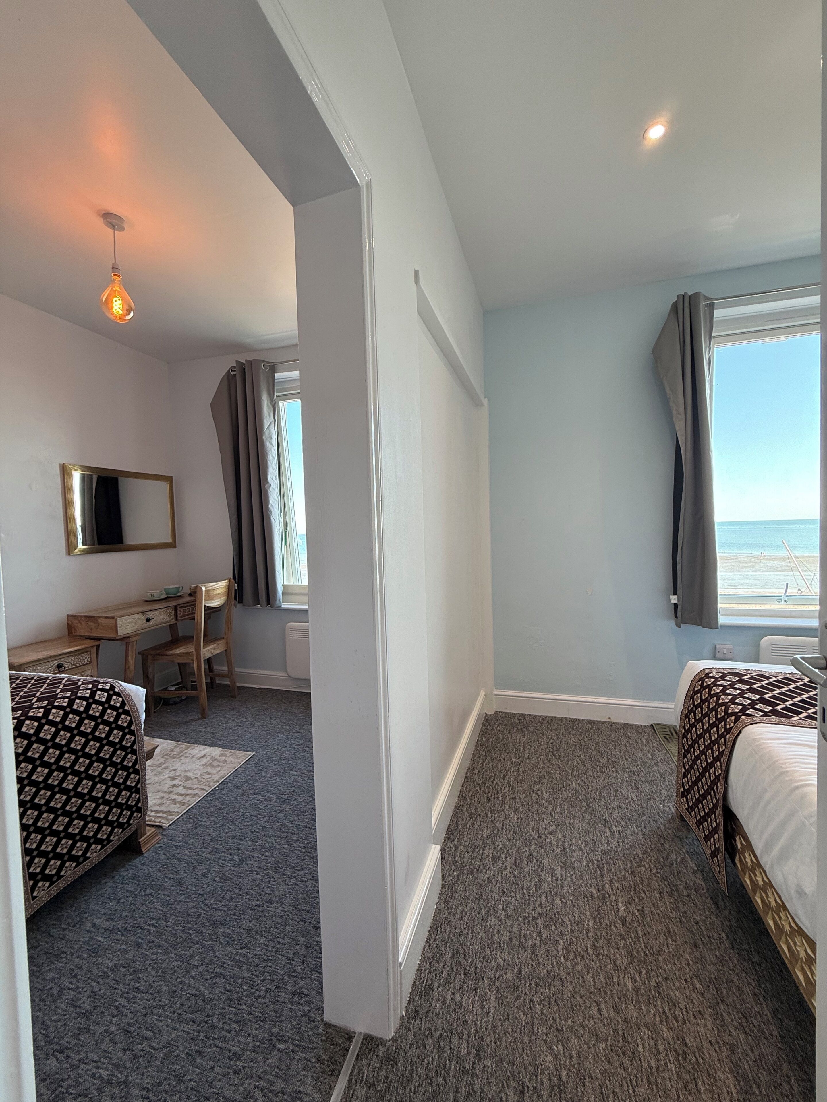 Habitación de hotel con cama, escritorio, silla, espejo y vista al mar.