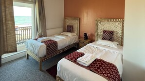 Hotellihuone, jossa on kaksi sänkyä, merinäköala ja kuviollinen sängynpääty.