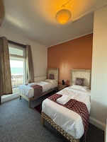 A hotel room with two beds, a view of the sea, and a patterned headboard.