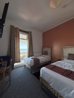 A hotel room with two beds, a desk, and a view of the sea.