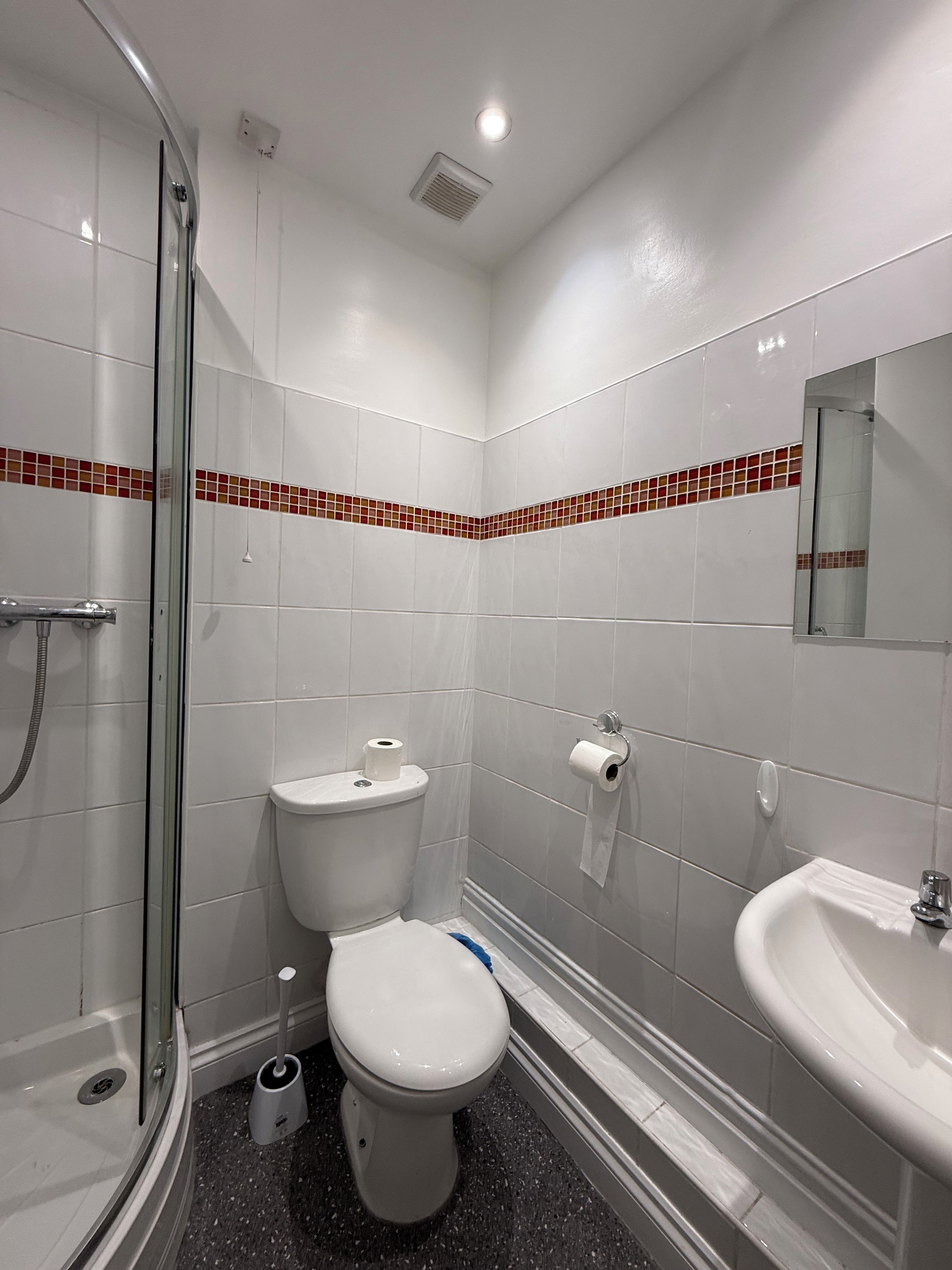 A bathroom with a glass shower enclosure, a toilet, a sink, and a mirror.