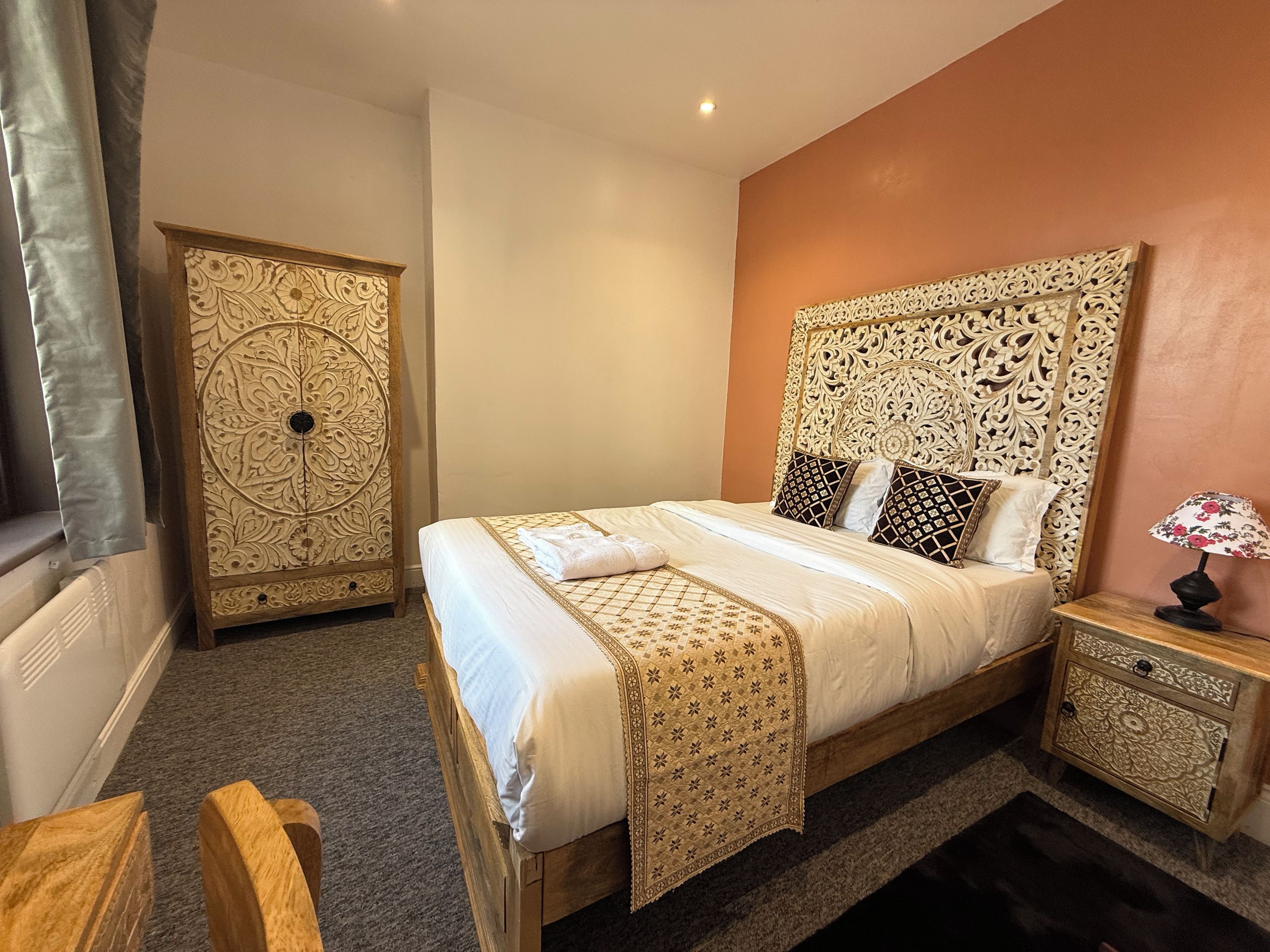 A bedroom with a bed, nightstand, and a decorative headboard.