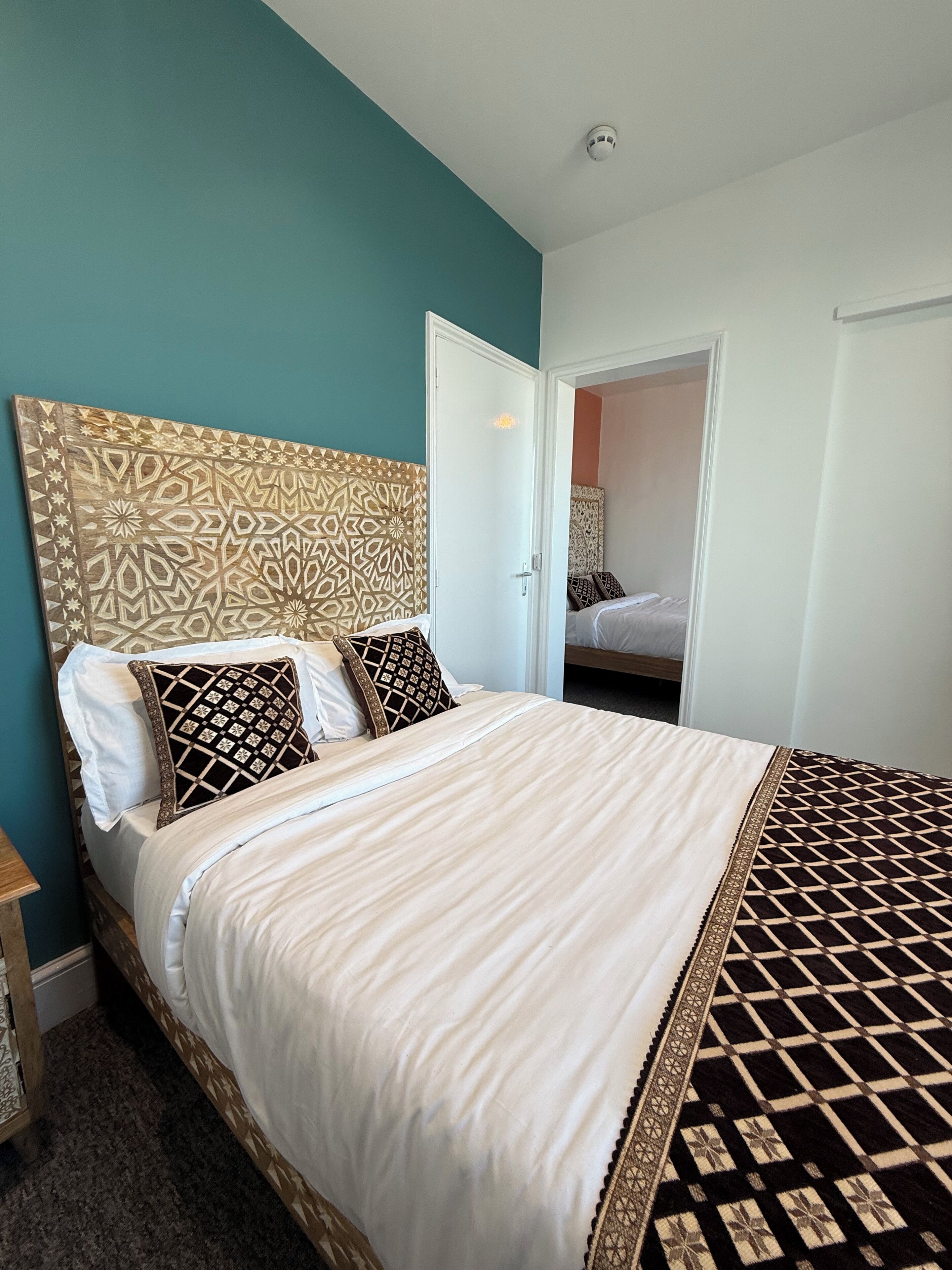 Ein Schlafzimmer mit einem gemusterten Kopfteil, einem Bett mit weißer Bettwäsche und einem gemusterten Teppich.