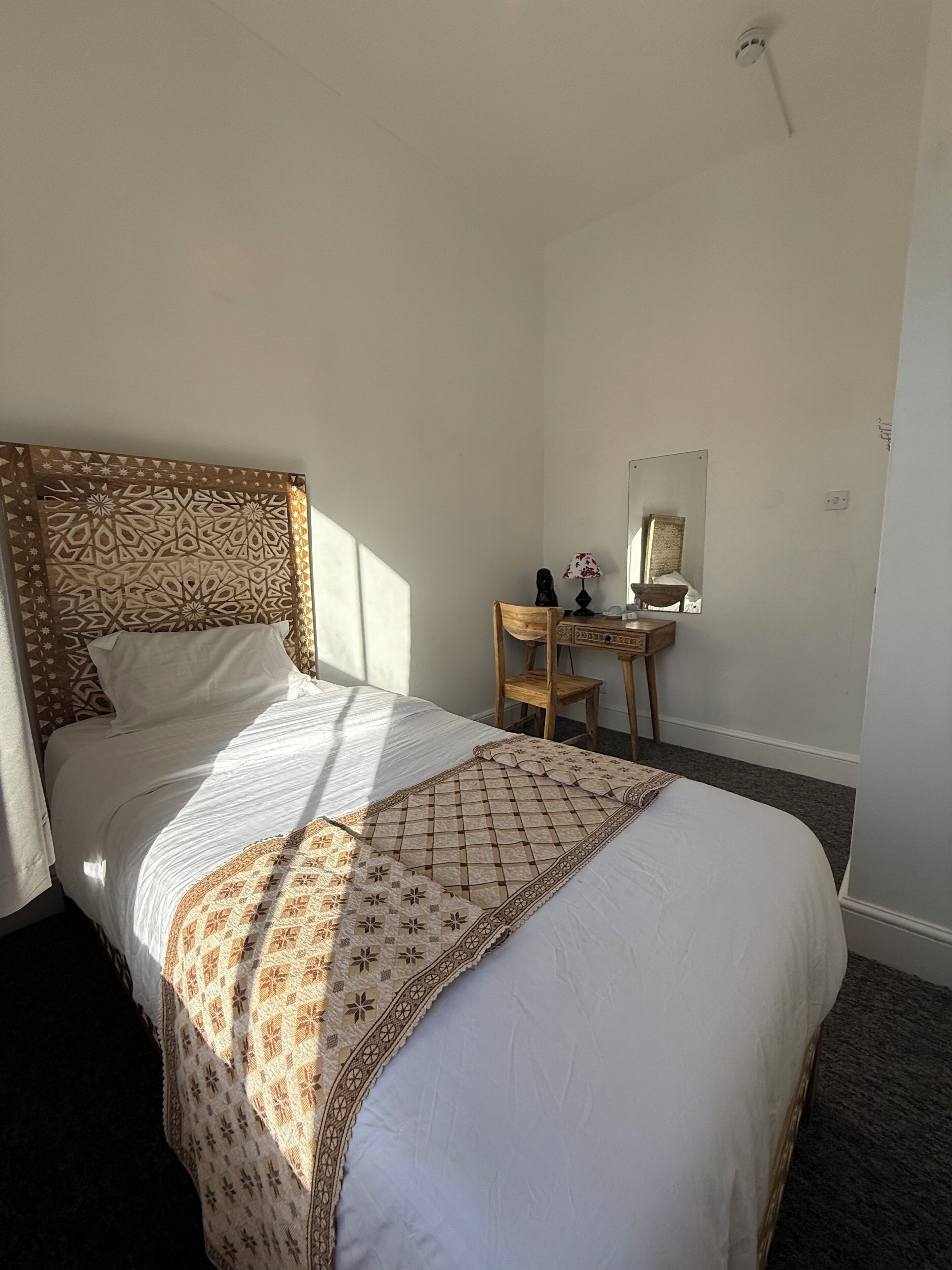 A hotel room with a neatly made bed, a wooden nightstand with a lamp, and a mirror on the wall.