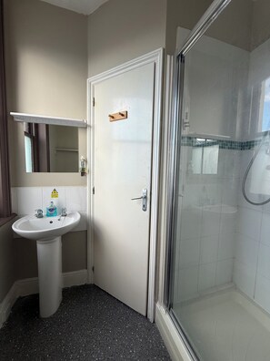 Un baño con lavamanos blanco, un espejo y cabina de ducha de vidrio.