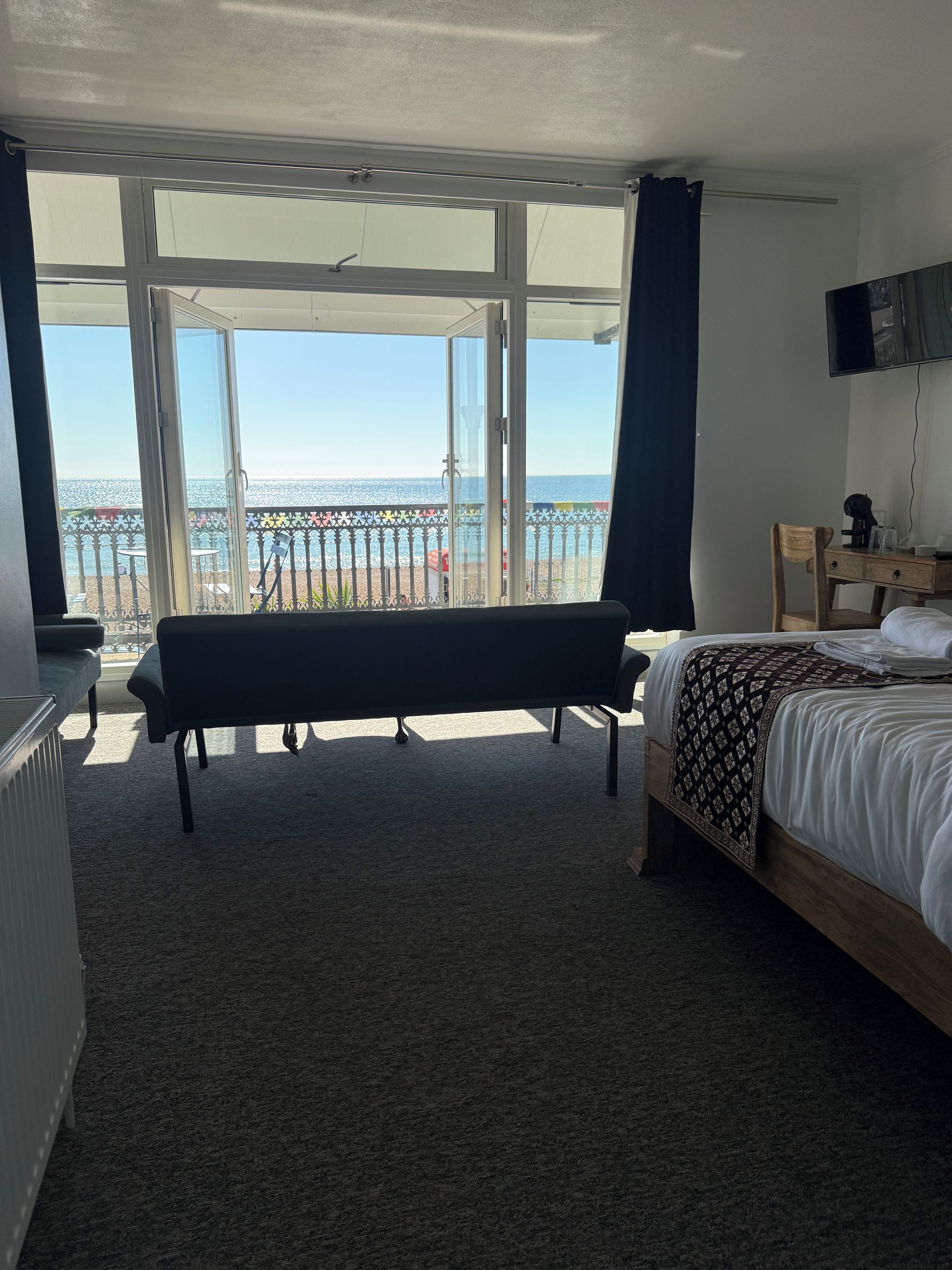 A hotel room with a bed, a bench, a desk, and a TV.