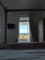 Un dormitorio con una cama grande, un televisor en la pared y un balcón con vista a la playa.