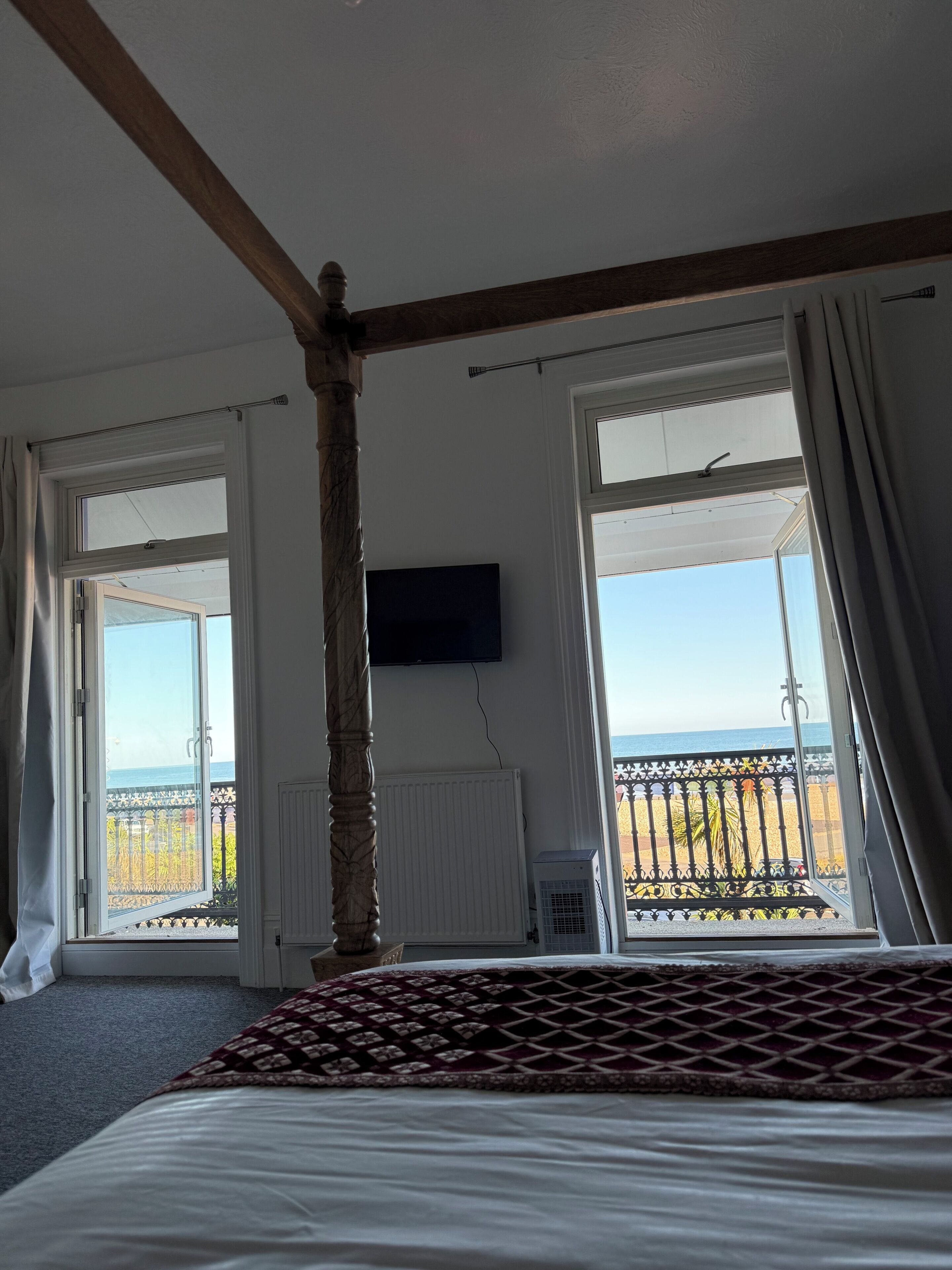 A room with a bed, a television, and large windows with a view of the sea.